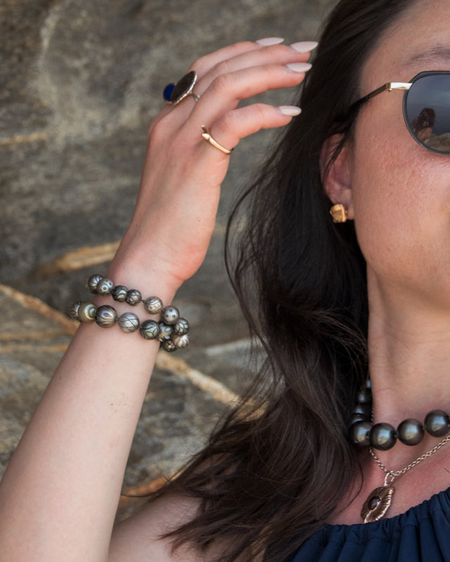 Person wearing necklace, featuring Tahitian pearl sculptures, against a caldera backdrop