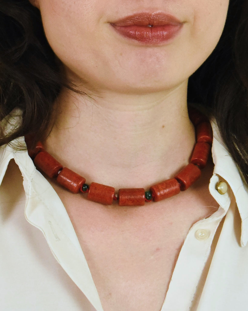 Person wearing a red beaded necklace with a white shirt