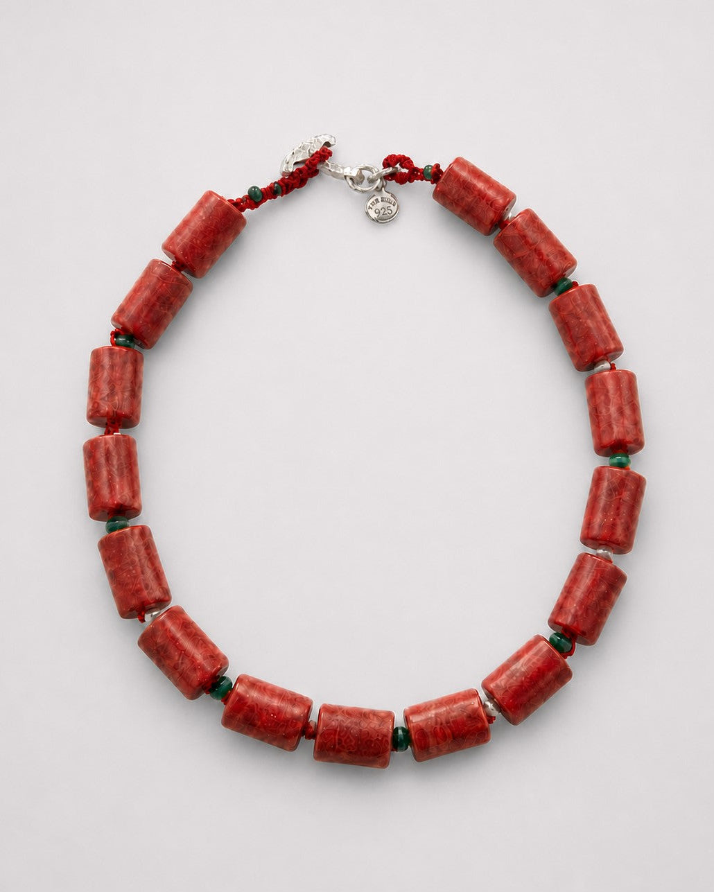 A beaded necklace made of cylindrical red coral-like beads separated by small dark green spacer beads, with a silver clasp and red cord, shown on a light gray background.