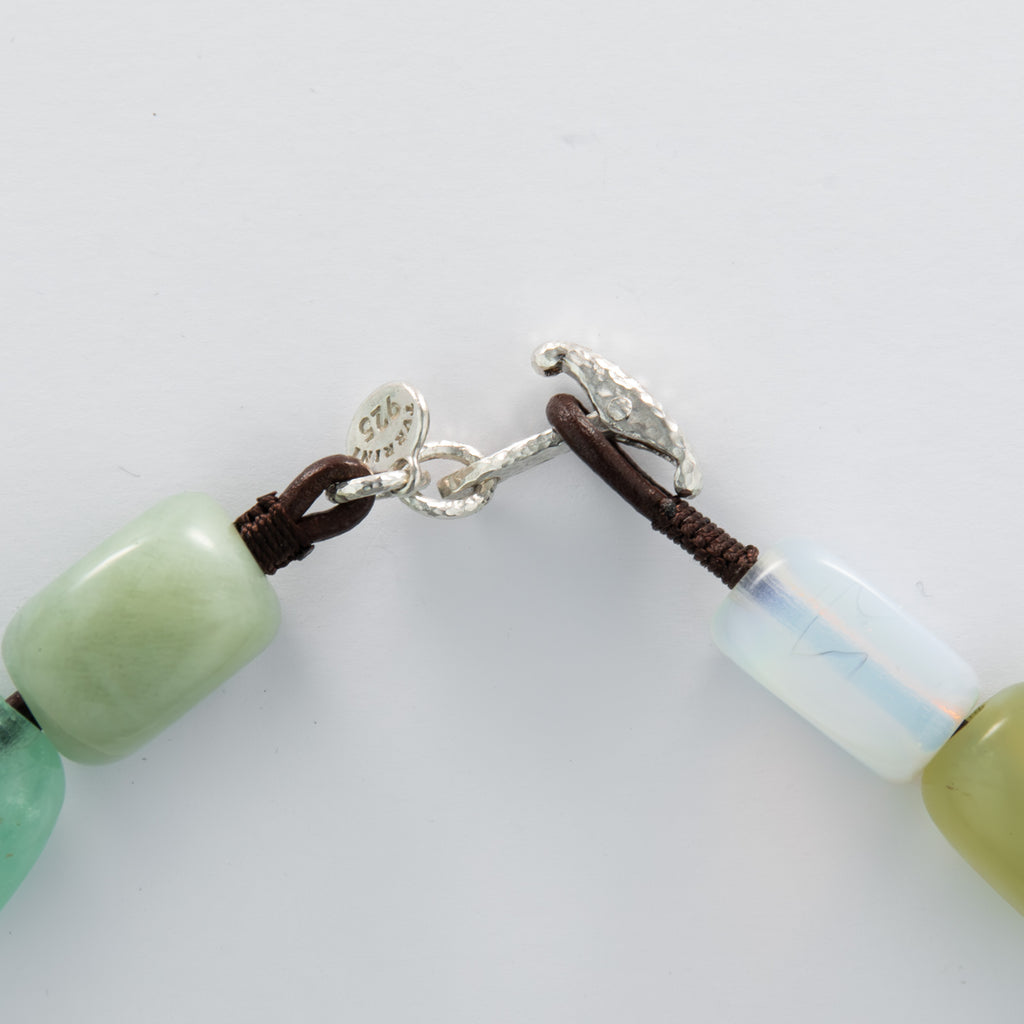 Close-up of a necklace with green beads and silver clasp on a plain white background