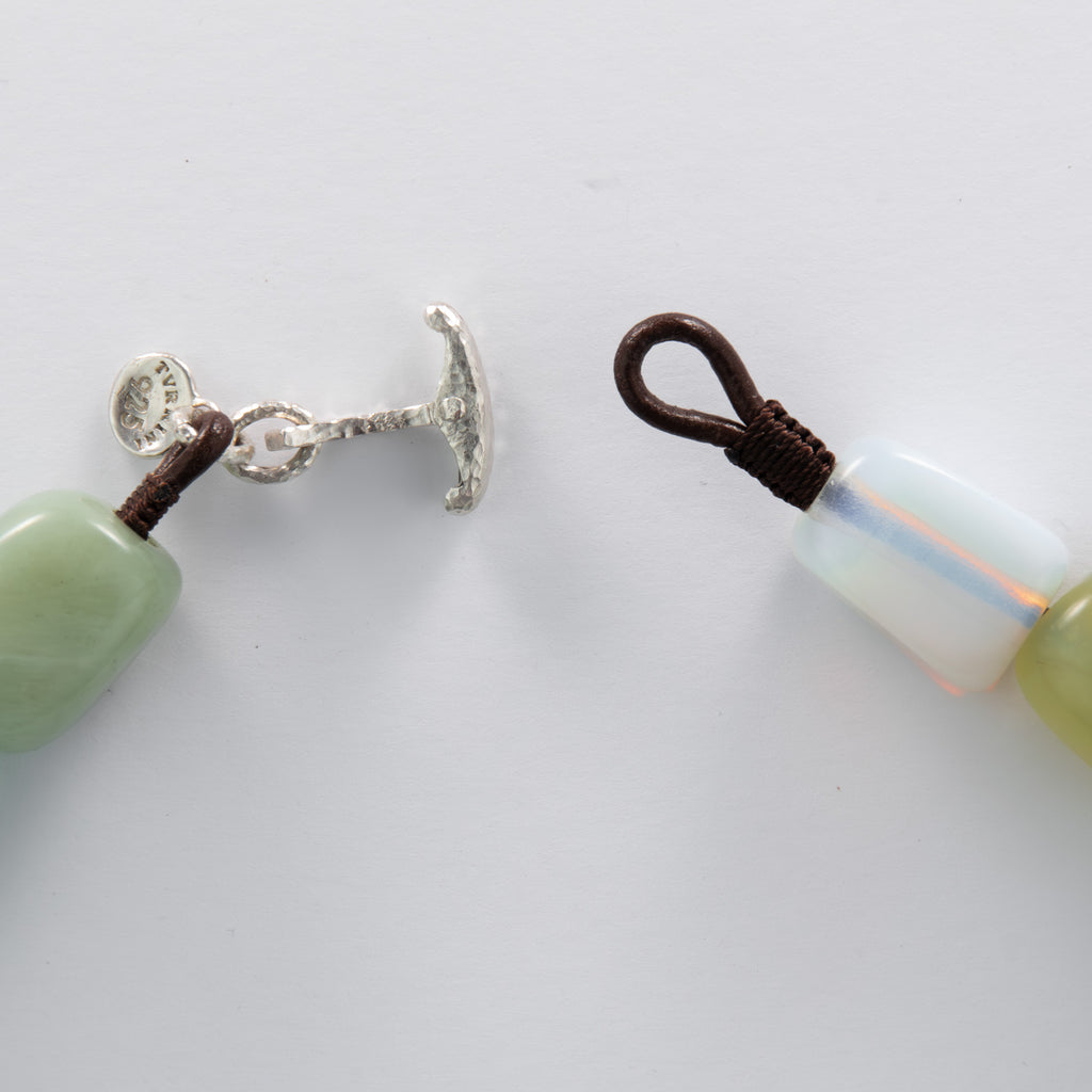 Close-up of a beaded necklace with silver clasp and brown cord on a white background