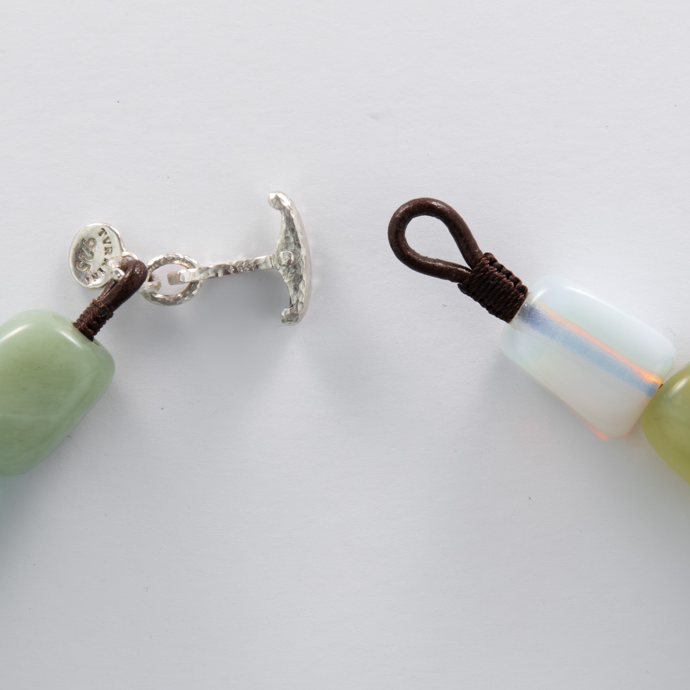 Close-up of a beaded necklace with silver clasp and brown cord on a white background