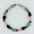 Beaded bracelet with green, pink, and black beads on a white background