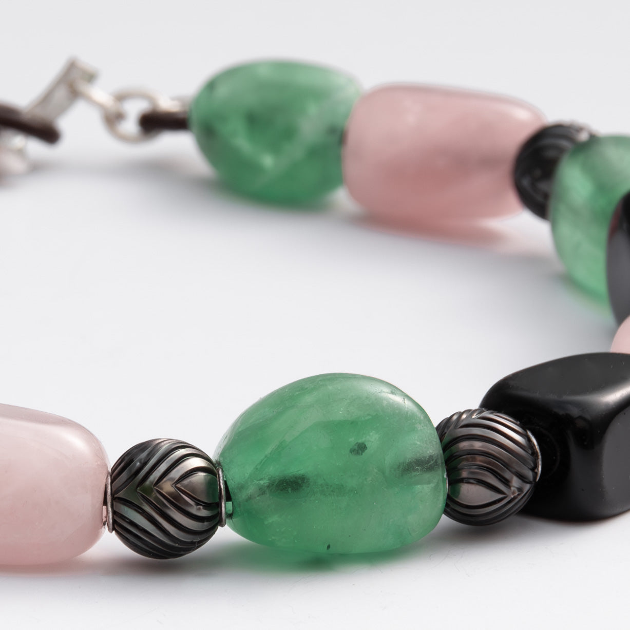 Close-up of a necklace with green, pink, and black beads on a white background