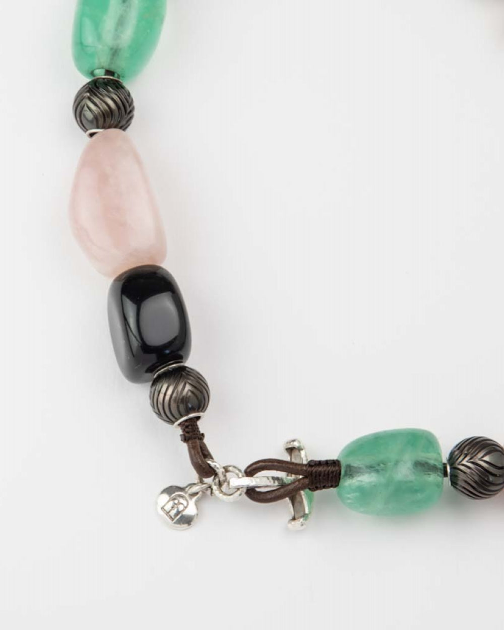 A close-up of a beaded necklace made with polished green, pink, and black beads, textured Tahitian pearls, and a silver toggled clasp.