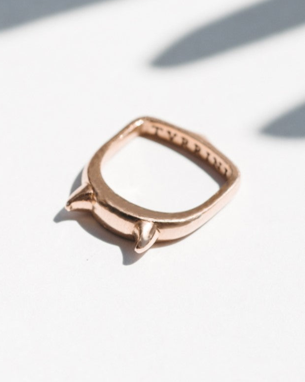 A rose gold ring featuring an elegant arch-shaped band with two small horns at the top, pack shot.