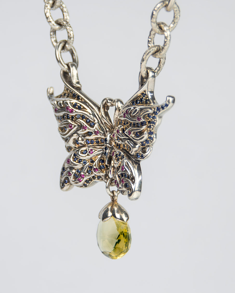 angled view of a butterfly-shaped silver pendant necklace, exhibiting the intricate stone-setting and high polish