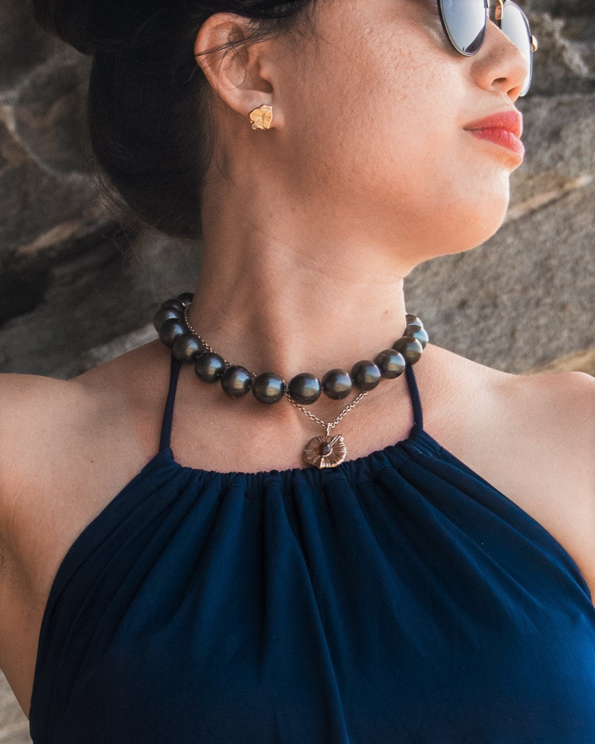 Close-up of a female model wearing a large Tahitian pearl choker, a delicate pendant on a chain, and citrine earring studs.