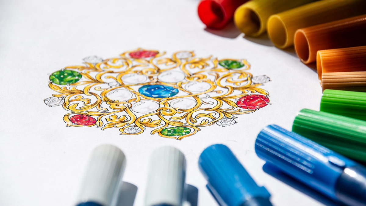 An intricate brooch design illustration surrounded by brush pens in rainbow colours