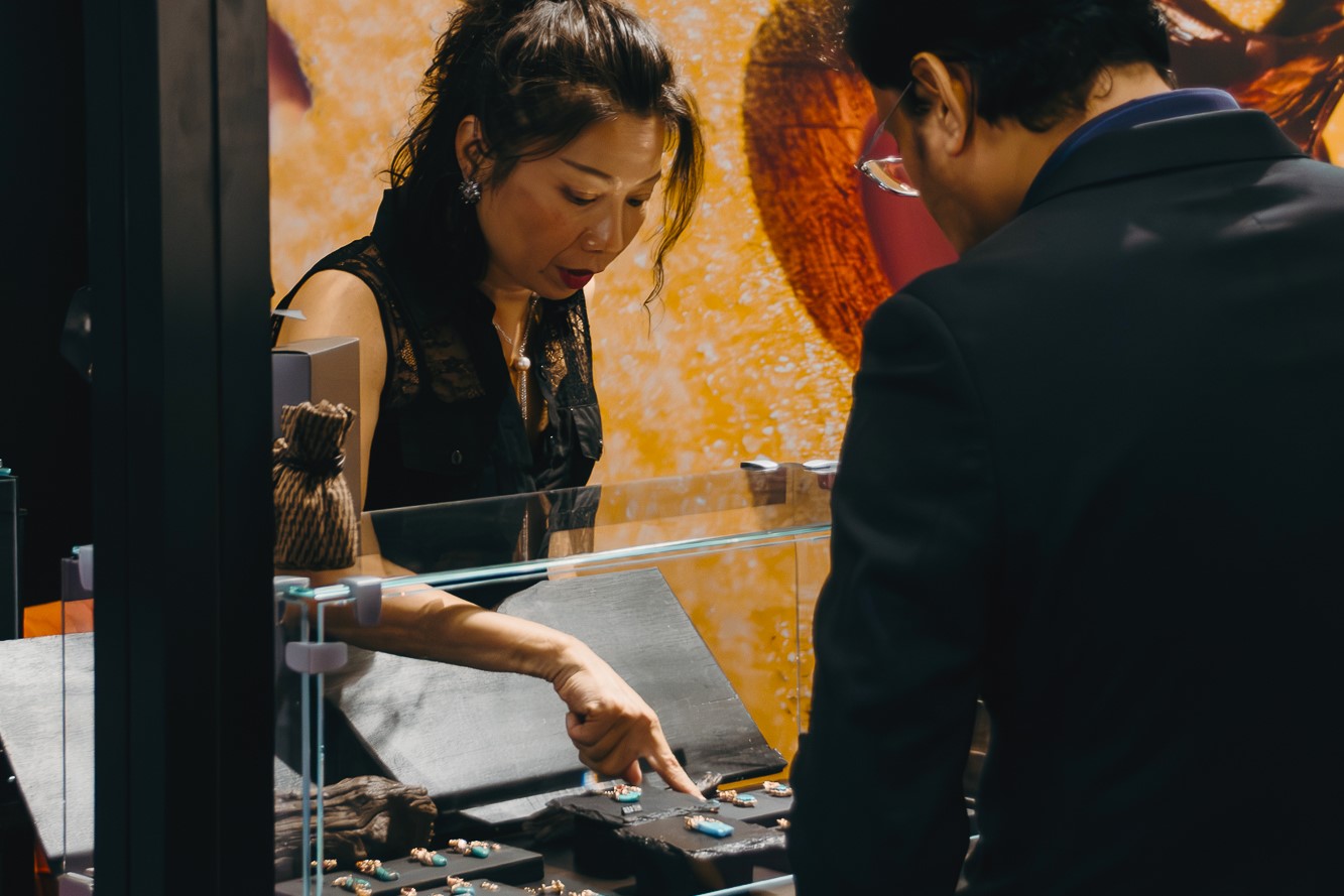 Bibi talking to a trade show visitor while both are looking at a Lava earring on display