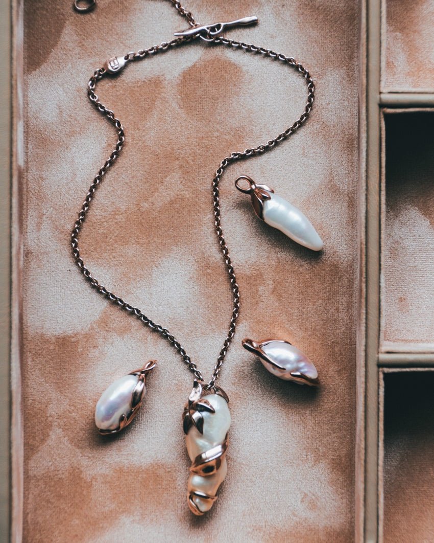 Four unique Kara 18K rose gold plated sterling silver and baroque freshwater pearl pendants sit in a jewellery box with TVRRINI chain