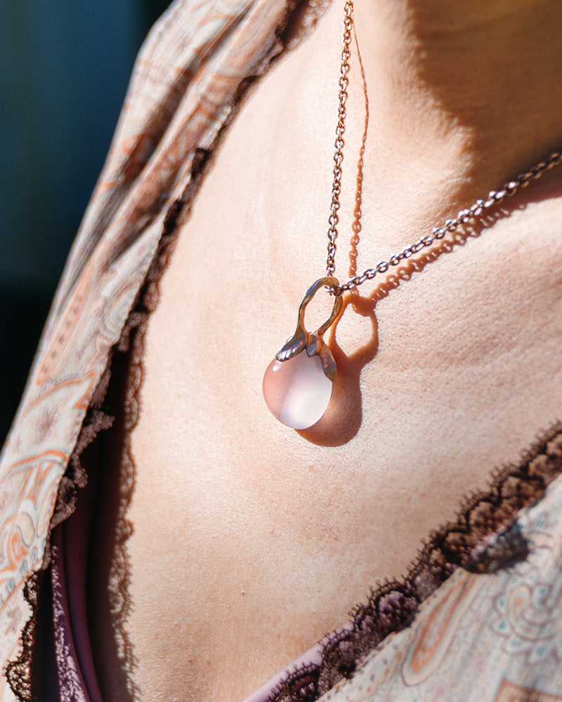 model wearing a gold-plated silver pendant, featuring rose quartz cabochon held by a free-form setting, natural sunlight enhancing the gemstone's glow