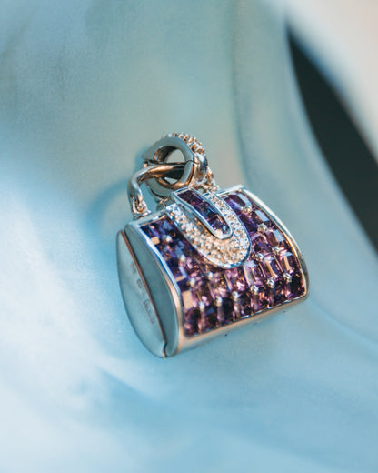 angled view of a pendant featuring amethyst and diamonds framed in a precise, handbag-shaped frame 