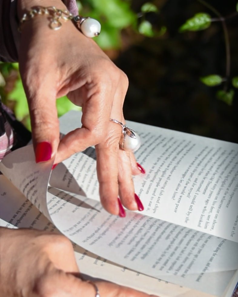 Model wearing unique Kara ring in sterling silver with freshwater pearl while holding paperback book