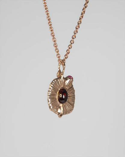 angled view of pendant, showcasing its sculpted, asymmetrical design and the soft glow of the central garnet cabochon