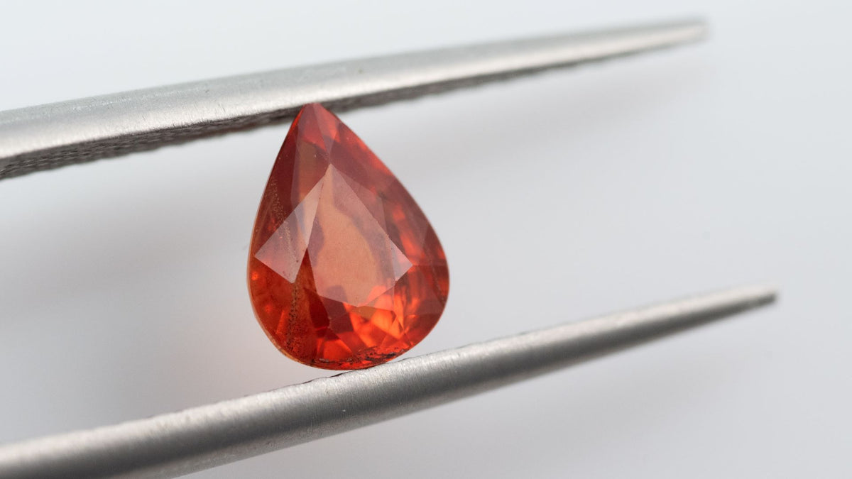 Gemstone tweezers presenting a pear-cut orange sapphire.
