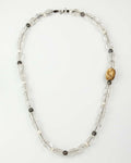 A beaded necklace made of clear quartz beads, freshwater pearls, Tahitian pearls, and a prominent carved bone on a white background.