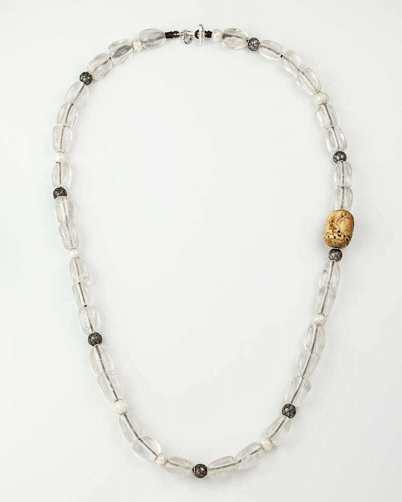 A beaded necklace made of clear quartz beads, freshwater pearls, Tahitian pearls, and a prominent carved bone on a white background.
