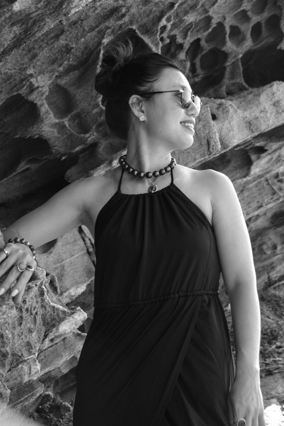 A woman in summer attire wearing fine jewellery while standing on a rocky cliff.