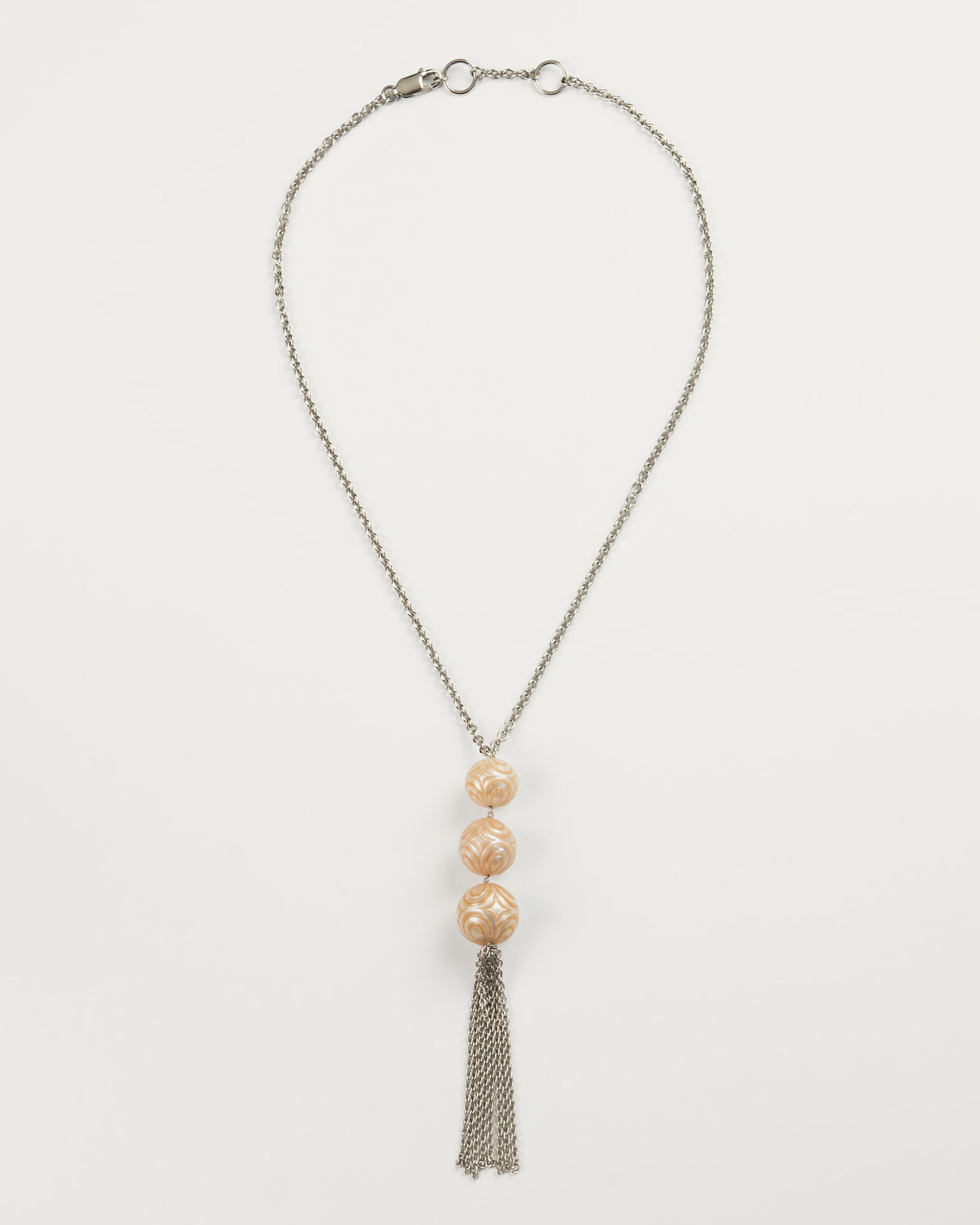 Silver chain necklace featuring three vertically aligned peach pearls with floral patterns, ending in a silver-toned tassel, against an off-white background.