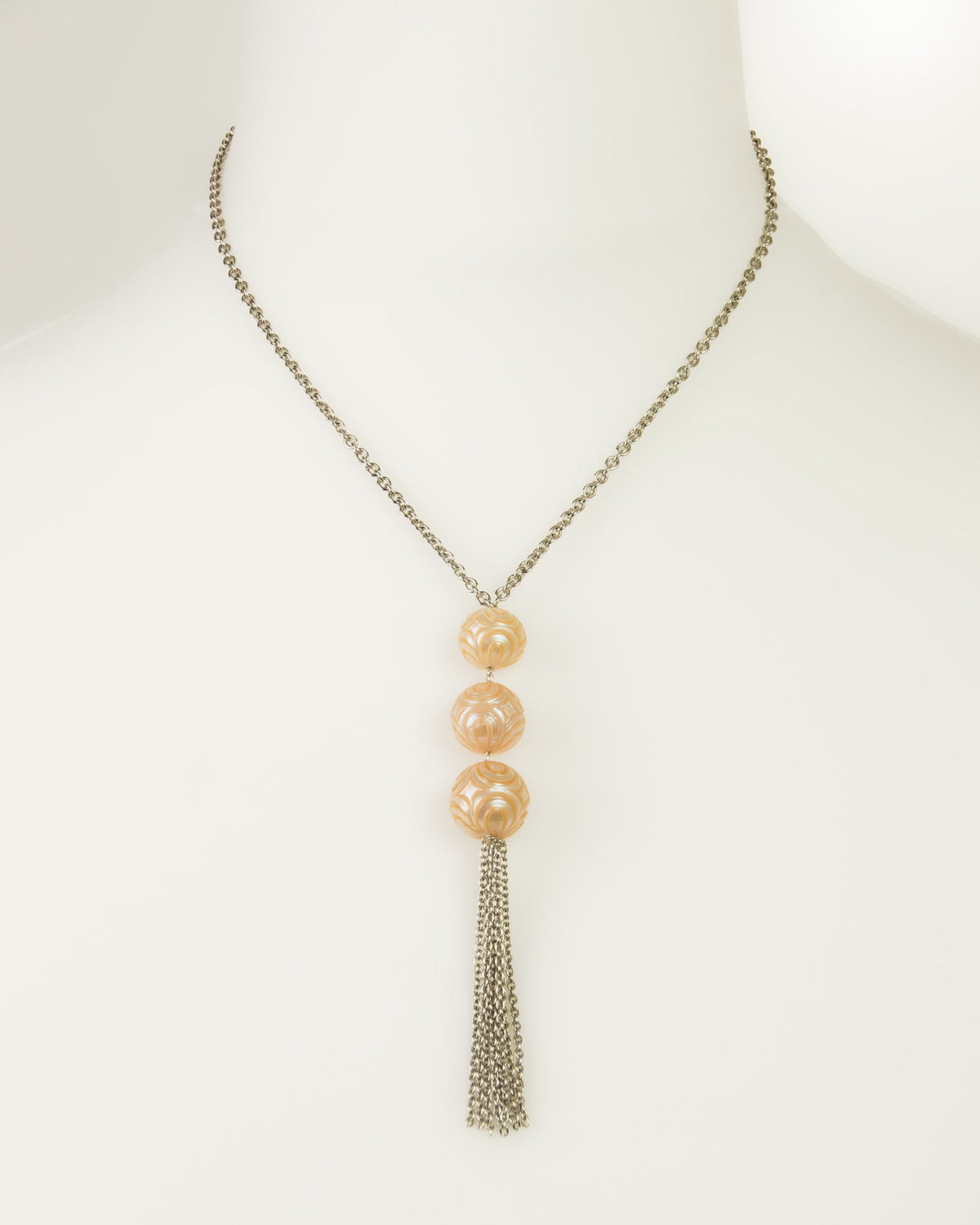 Silver chain necklace displayed on a white mannequin, featuring three vertically aligned freshwater pearls center of the pendant, with a silver tassel