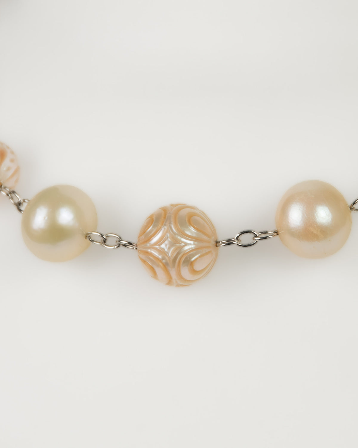 Close-up of chain necklace featuring large cream-colored pearls, plain and engraved, connected by silver links.