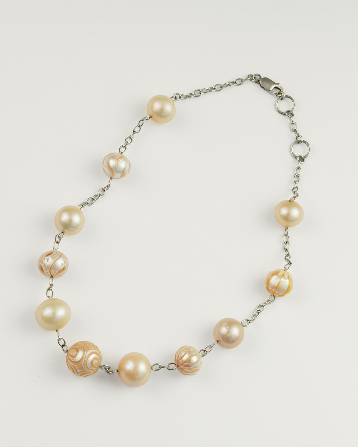 A silver chain necklace featuring a mix of large, cream-colored freshwater pearls and engraved pearls.