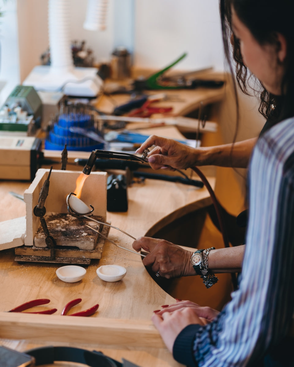 One person firing a crucible while a second one observes in a jewellery workshop