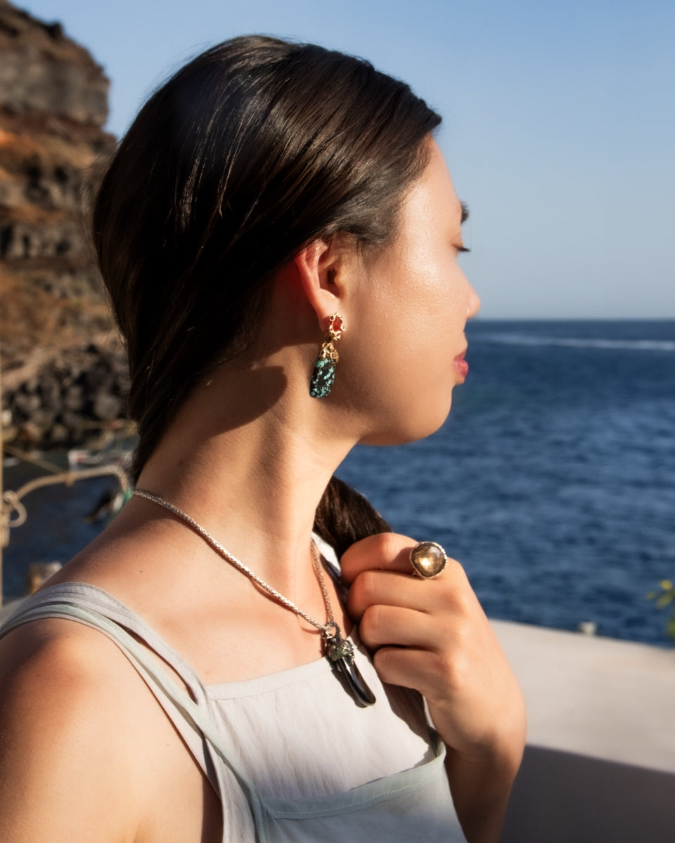 Katerina modelling three TVRRINI jewellery pieces while turning towards sun in Santorini
