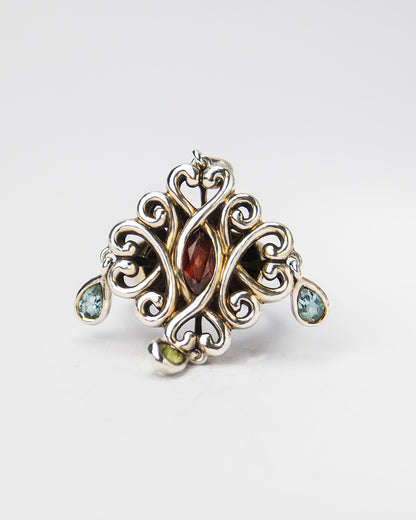 front of a silver ring, featuring garnet, blue topaz, and peridot framed by intertwining designs