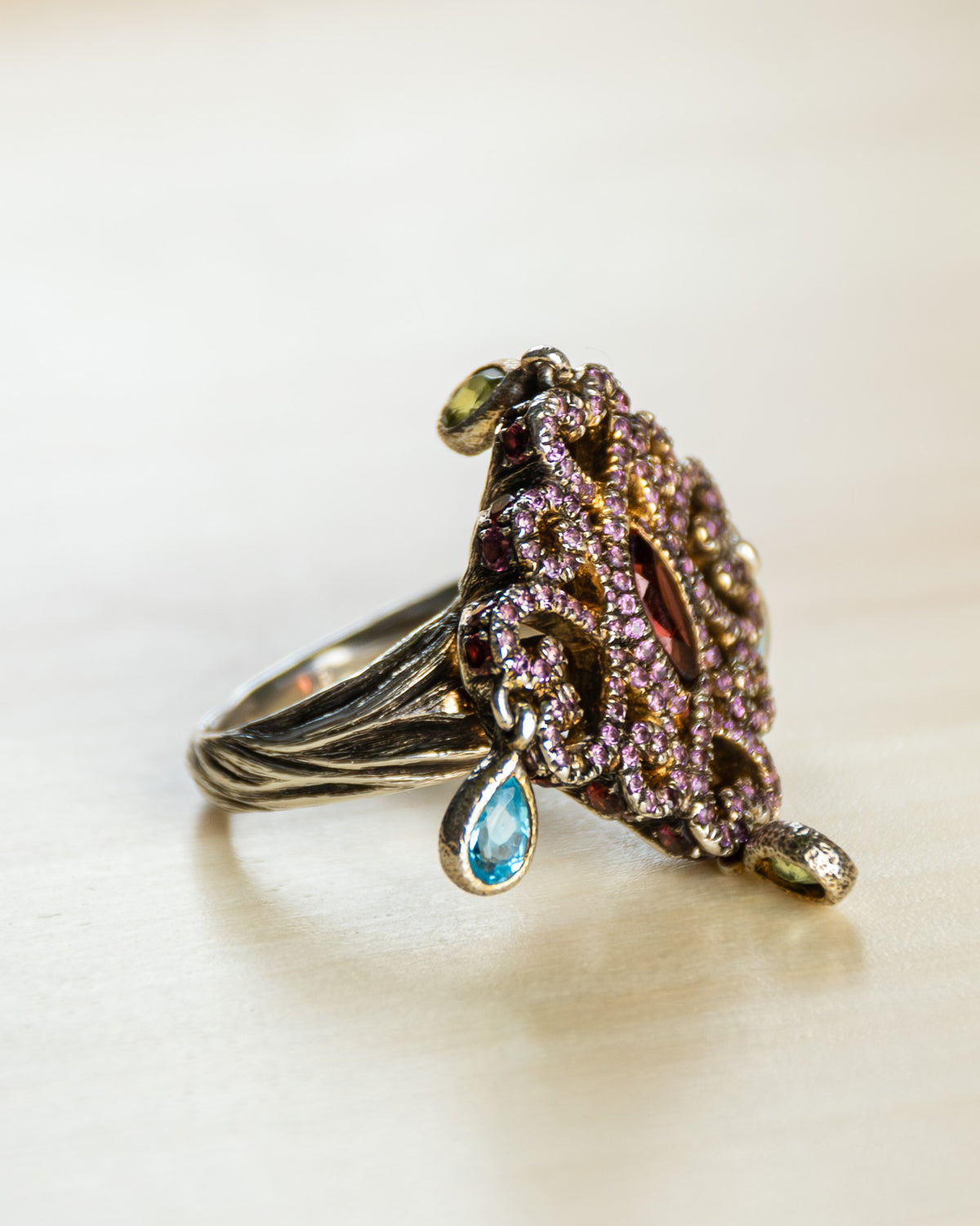 Silver ring embellished with assorted coloured gemstones set against a hand-textured shank oxidised for added detail.