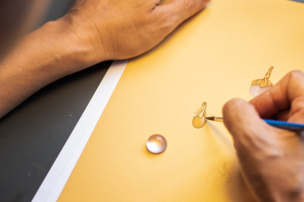Person drawing a small circle on a yellow sheet of paper with a paintbrush