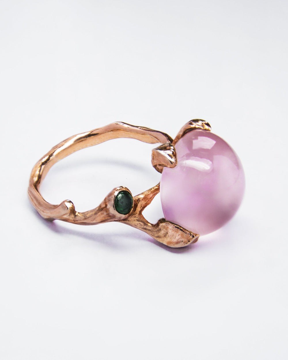 angled view of a unique ring, showcasing emerald side stone complementing the rose quartz central stone in an organic, abstract setting 