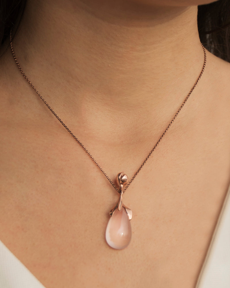 person wearing a sterling silver pendant with flower setting, featuring a rose quartz teardrop cabochon