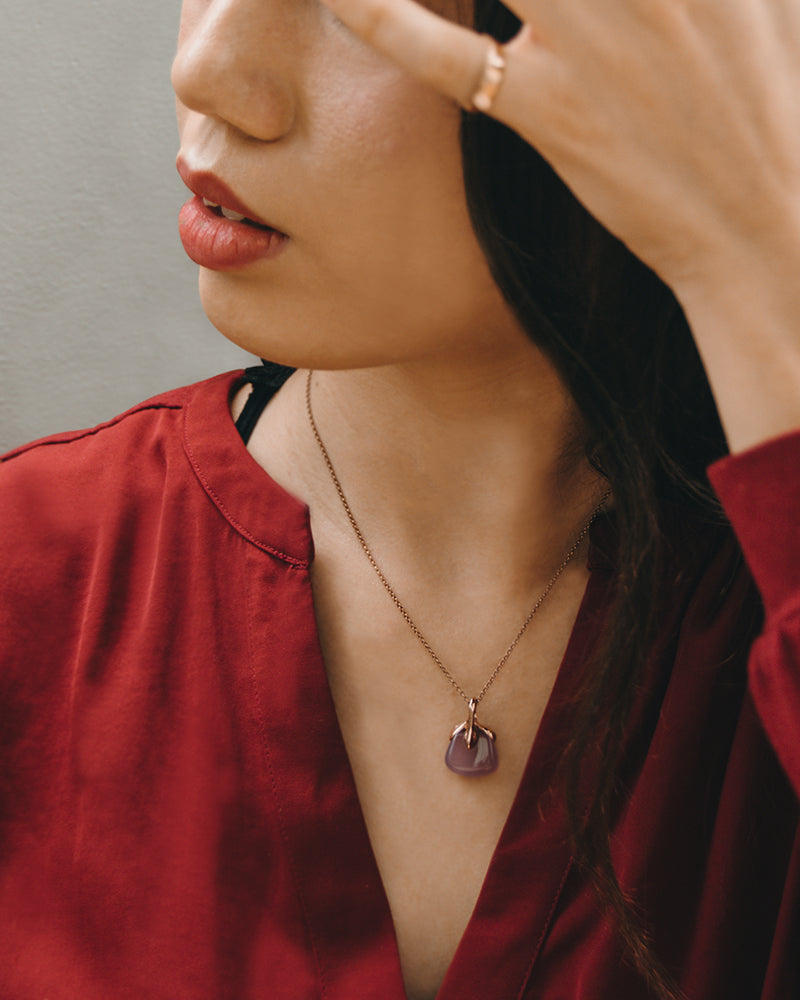 A model wearing a sterling silver pendant with a free-form design and a purple chalcedony, captured in an urban outdoor setting, complementing her casual style