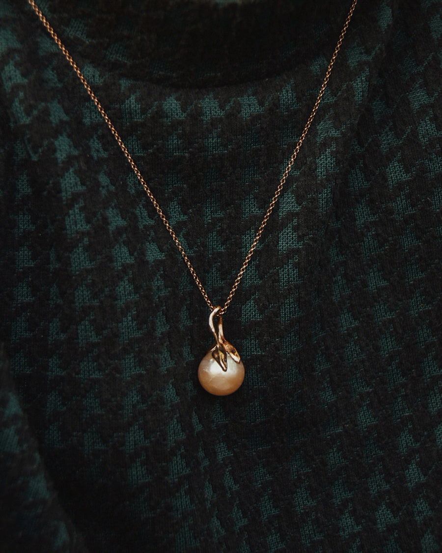Close-up of model wearing a pearl pendant with a free-form sculpted silver design, plated on with rose gold
