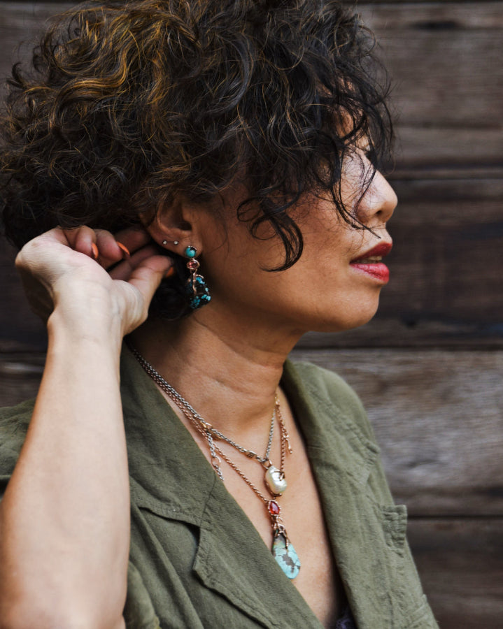 Bibi wearing Lava earrings with Lava pendant and Kara freshwater pearl pendant, enhanced by natural lighting in an outdoor setting