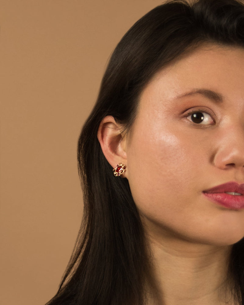 close-up of model wearing 18K rose gold stud earrings, featuring orange sapphire, ruby and diamond 