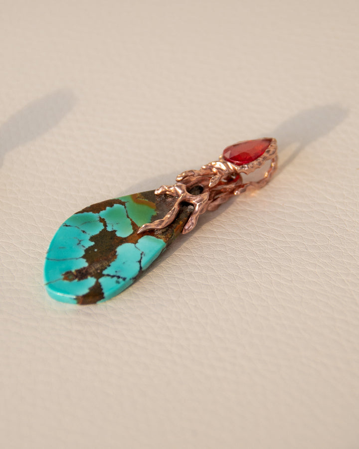 angled view of a pendant with a free-form gold-plated silver setting, showcasing the molten design and bold colours of the turquoise and orange sapphire