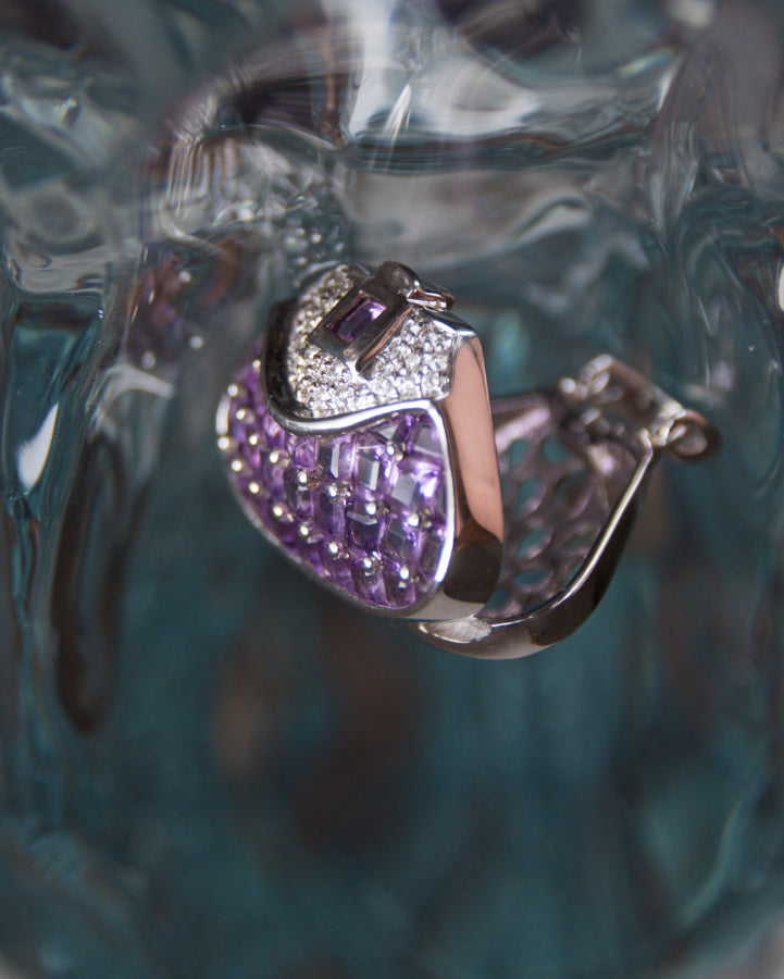 angled view of an open locket pendant with a meticulous white gold setting, displaying its careful design and sparkle of amethysts and diamonds