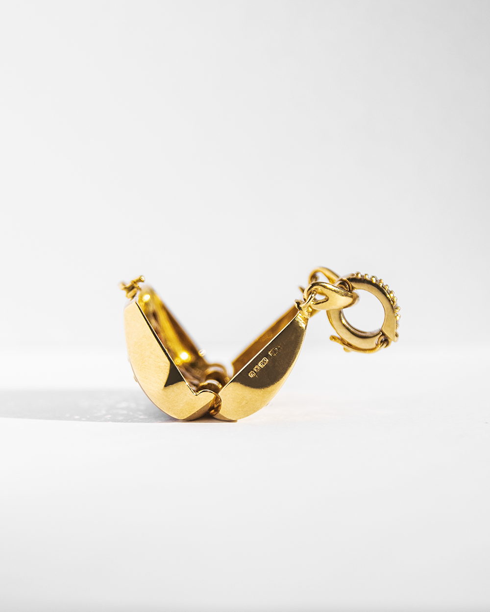 side profile of an 18K gold locket, showcasing its sleek hinged design, hallmark and smooth edges for a timeless  look