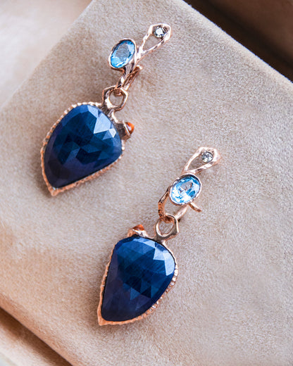 an overhead view of detachable earrings featuring blue and orange sapphires set in an abstract gold-plated silver setting, matched with hoops of the same metal