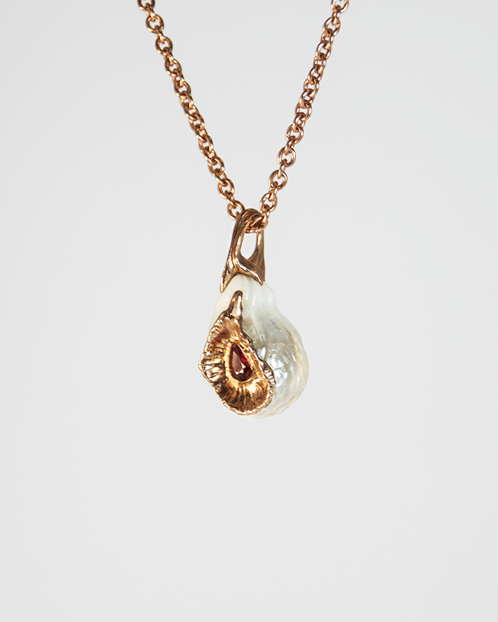 angled view of a pendant with a free-form gold-plated silver setting, highlighting its abstract design and pear-cut orange sapphire in the centre of a baroque freshwater pearl