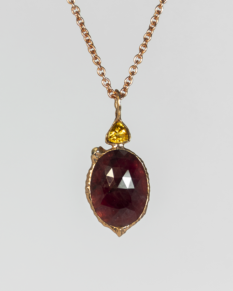 front view of a reversible pendant in 18K rose gold-plated silver cradling a ruby in the centre with citrine and moonstone accents
