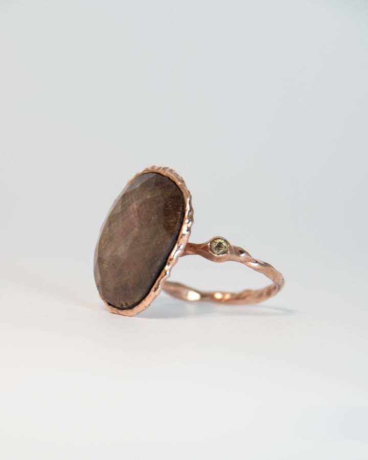 angled view of a ring with a free-form gold-plated silver setting, displaying its sculpted design and the central gold-sheen sapphire beside a side diamond