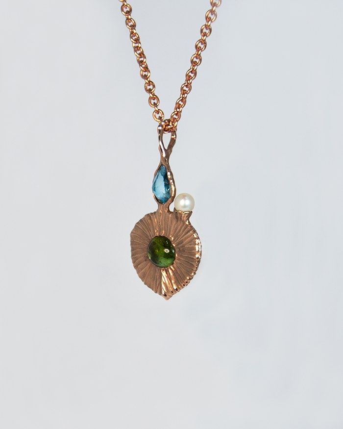 angled view of gold-plated silver pendant, highlighting textured setting that holds the blue topaz, green tourmaline, and freshwater pearl