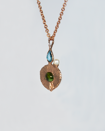 angled view of gold-plated silver pendant, highlighting textured setting that holds the blue topaz, green tourmaline, and freshwater pearl