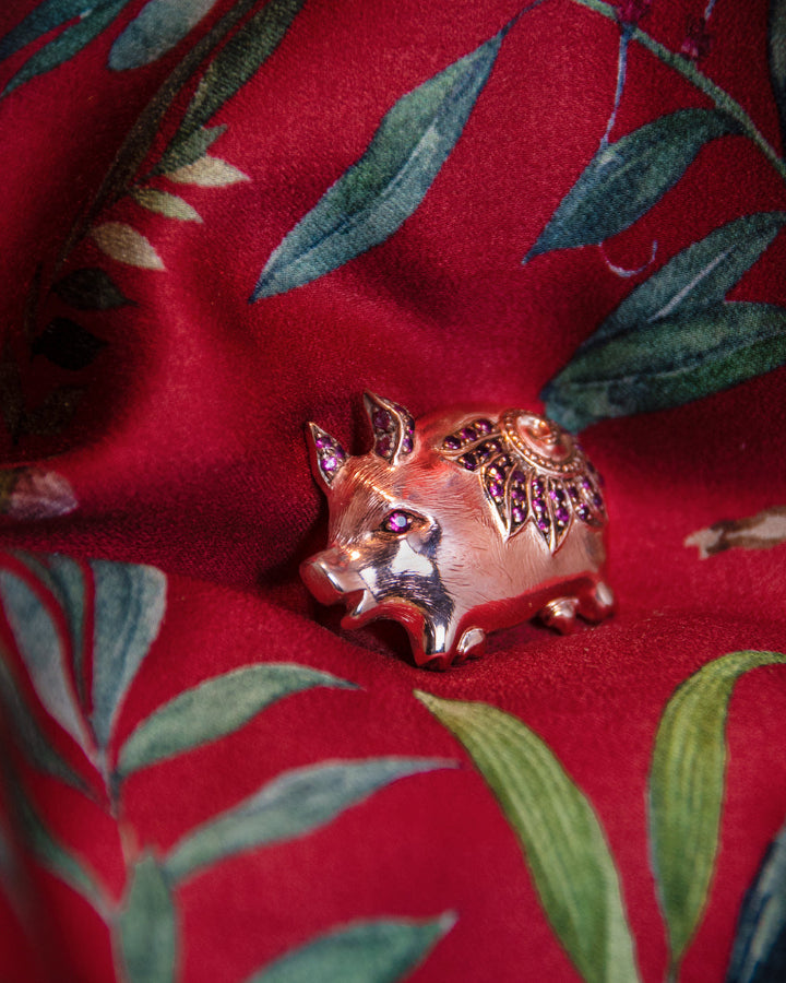 angled view of a pig-shaped pendant in sterling silver with rose gold plating, featuring rubies